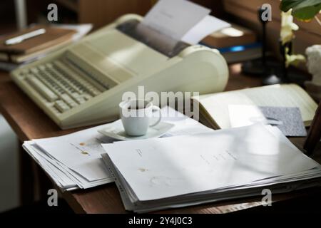 Klassische Schreibmaschine auf Holzschreibtisch mit Papierstapeln und Kaffeetasse. Die Szene weist darauf hin, dass Sie mit verschiedenen Dokumenten arbeiten oder im Büro arbeiten Stockfoto