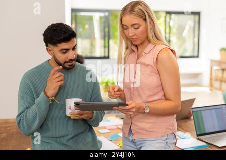 Über das Projekt diskutieren, junge Freunde, die ein Tablet verwenden und im Büro eine Kaffeetasse halten, Unternehmen gründen Stockfoto