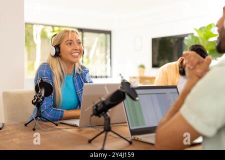 Podcast aufnehmen, Frau trägt Kopfhörer und lächelt mit Laptop und Mikrofonen Stockfoto