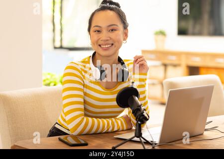 Lächelnde Frau mit Kopfhörern, die Podcasts mit Laptop und Mikrofon aufnimmt Stockfoto