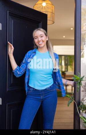 Lächelnde junge Frau, die vor der Tür steht, mit blauem Hemd und Jeans Stockfoto