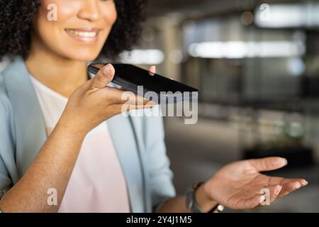 Smartphone in der Hand, Geschäftsfrau lächelnd und mit Sprachassistent im Büro Stockfoto