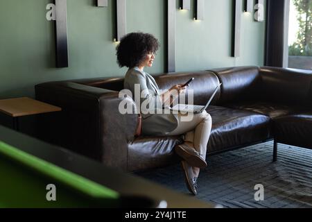 Mit Smartphone und Laptop, Frau, die von der modernen Bürolounge aus arbeitet Stockfoto