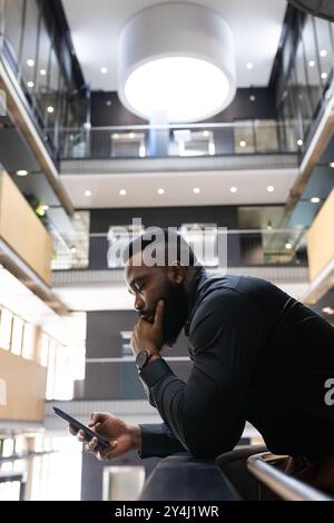 Mit Smartphone konzentriert sich afroamerikanischer Geschäftsmann auf die Arbeit im modernen Büro, Kopierraum Stockfoto