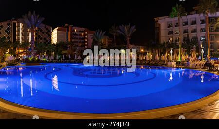 Alanya, Türkei - 17. September 2021: Eine schöne nächtliche Szene eines großen, beleuchteten Hotelpools, umgeben von Palmen und moderner Architektur, Stockfoto