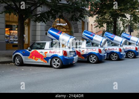 Prag, CZ - 10.08.2024: Red Bull-Werbekampagne in Prag zeigt Mini Cooper-Autos mit Markenzeichen, die auf einer Straße mit Boutiquen geparkt sind. Stockfoto