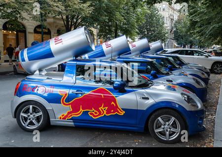 Prag, CZ - 10.08.2024: Red Bull-Werbekampagne in Prag zeigt Mini Cooper-Autos mit Markenzeichen, die auf einer Straße mit Boutiquen geparkt sind. Stockfoto