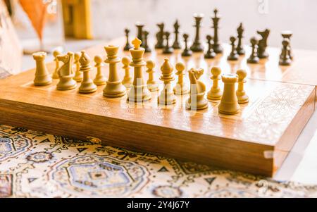 Schachbrett mit ordentlich angeordneten Schachfiguren auf Holztisch im Sonnenlicht, bereit für ein Spiel, strategisches Denkkonzept Stockfoto