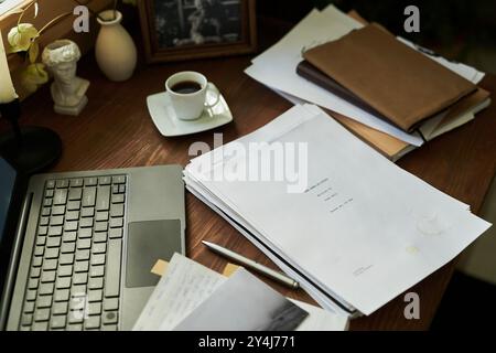 Übersichtliche Einrichtung im Home Office mit Laptop, Kaffeetasse und Papierstapel, die ordentlich auf dem Schreibtisch platziert sind. Gemütlicher, von einer Lampe beleuchteter Arbeitsbereich für produktive Arbeit Stockfoto