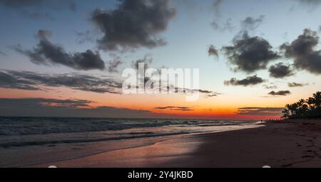 Bavaro Beach bei Sonnenaufgang, Dominikanische Republik. Panoramablick auf Küstenlandschaften mit aufsteigender Sonne und Palmen-Silhouetten unter farbenfrohem Himmel Stockfoto