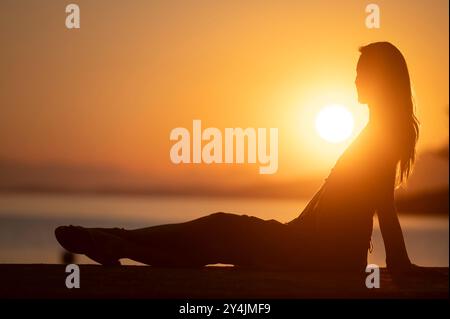 Profilansicht einer jungen Frau, die am Meer bei schönem Sonnenaufgang sitzt und ihren Urlaub genießt und sich entspannt. Stockfoto