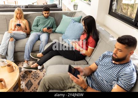 Mit Smartphones sitzen junge Freunde zusammen auf der Couch im Wohnzimmer Stockfoto