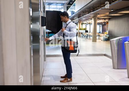 Geschäftsmann mit Aktenkoffer, der die Fahrstuhltaste in einem modernen Bürogebäude drückt Stockfoto