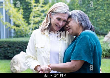 Im Garten, umarmt und lächelt, genießen hochrangige, multirassische Freundinnen die gemeinsame Zeit im Freien Stockfoto