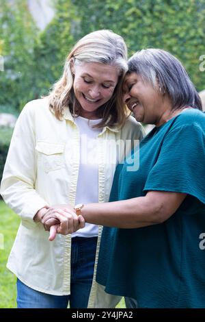 Im Garten, lächelnde ältere, multirassische Freundinnen, die Hände halten und die gemeinsame Zeit genießen Stockfoto