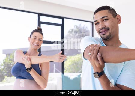 Multirassisches Paar, dehnt sich zusammen, schwangere Frau und Mann lächeln während des Heimtrainings Stockfoto