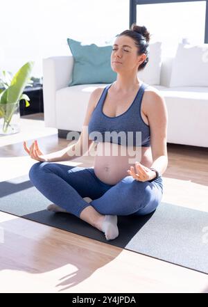 Zu Hause, schwangere Frau meditiert auf Yogamatte im Wohnzimmer, übt Achtsamkeit Stockfoto