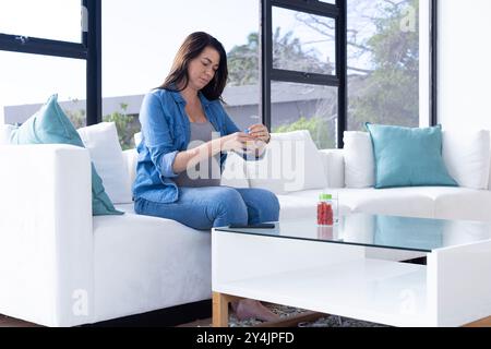 Zu Hause sitzt eine schwangere Frau auf der Couch und nimmt pränatale Vitamine aus der Flasche Stockfoto