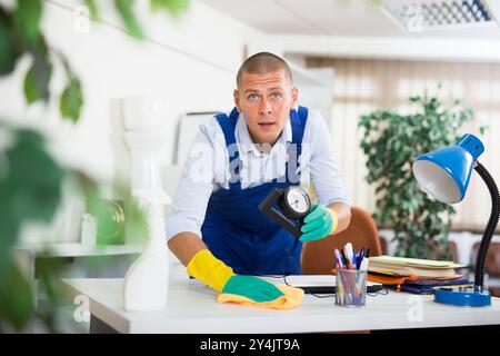 Qualifizierte Hausmeister Staubwischen Möbel im Büro mit Reinigungsgeräten Stockfoto