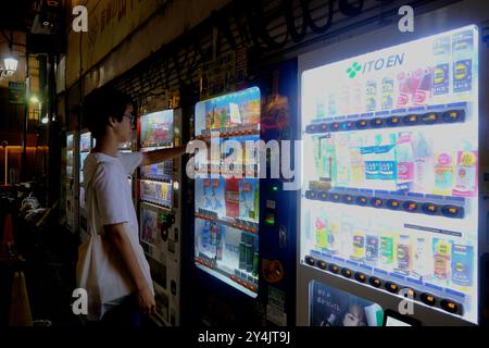 Junger Mann, der in der späten Nacht alkoholfreie Getränke aus einem Automaten auf dem Bürgersteig kauft. Ebisu, Shibuya Bezirk. Tokio, Japan Stockfoto