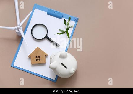 Klemmbrett mit Pflanze, Lupe, Hausfigur, Schweinebank und Windturbine auf braunem Hintergrund. Konzept der grünen Energie Stockfoto