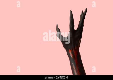 Schwarze Hexenhand mit Krallen auf rosa Hintergrund. Halloween-Feier Stockfoto