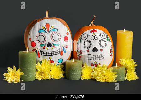 Kürbisse mit bemalten Schädeln, brennenden Kerzen und wunderschönen Blumen auf dunklem Hintergrund. El Dia de Muertos Stockfoto