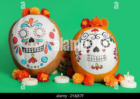 Kürbisse mit bemalten Schädeln, Ringelblumen und brennenden Kerzen auf grünem Hintergrund. El Dia de Muertos Stockfoto