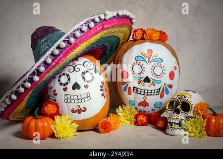 Kürbisse mit bemalten Schädeln, Sombrero und Blumen auf hellem Hintergrund. El Dia de Muertos Stockfoto