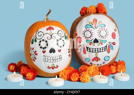 Kürbisse mit bemalten Schädeln, wunderschönen Ringelblumen und brennenden Kerzen auf farbigem Hintergrund. El Dia de Muertos Stockfoto