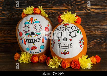 Kürbisse mit bemalten Schädeln und schönen Blumen auf hölzernem Hintergrund. El Dia de Muertos Stockfoto