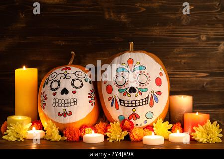 Kürbisse mit bemalten Schädeln, brennenden Kerzen und Blumen auf hölzernem Hintergrund. El Dia de Muertos Stockfoto