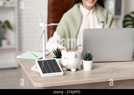 Windturbinenmodell mit Solarpanel, Schweinebank und Anlagen auf dem Tisch der Ingenieurin im Büro, Großaufnahme Stockfoto