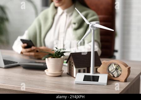 Windkraftanlage mit Hausmodell, Schweinebank und Anlage auf dem Tisch der Ingenieurin im Büro, Großaufnahme Stockfoto