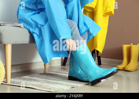 Frau mit Regenmantel, die Gummistiefel im Flur anzieht Stockfoto