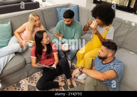 Eine Gruppe junger Freunde sitzt auf der Couch, trinkt Kaffee und redet miteinander Stockfoto