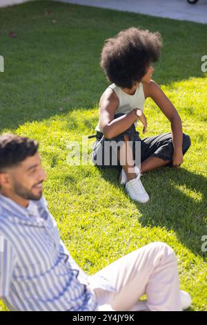 Freunde sitzen auf Gras, genießen den sonnigen Tag und entspannen sich im Freien Stockfoto