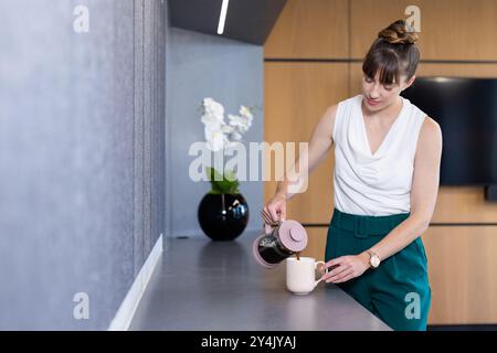 Kaffee aus der französischen Presse in den Becher gießen, Frau im Büro, Kopierraum Stockfoto