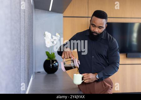 Kaffee in die Tasse gießen, afroamerikanischer Geschäftsmann macht Pause in der modernen Büroküche Stockfoto