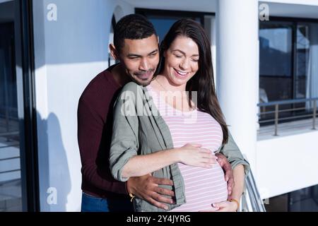 Auf dem Balkon, einnehmend, glückliches multirassisches Paar, das den Moment genießt, zusammen ein Baby erwartet, lächelnd Stockfoto
