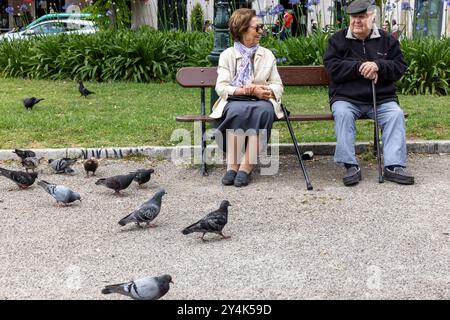 Ein älteres Ehepaar, das auf einer Parkbank sitzt und Tauben füttert, in Lissabon, Portugal Stockfoto