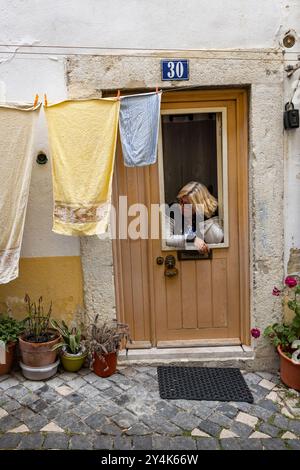 Eine Frau in der Tür ihres Hauses mit Wäsche, die an einer Wäscheleine hängt, in Lissabon, Portugal Stockfoto