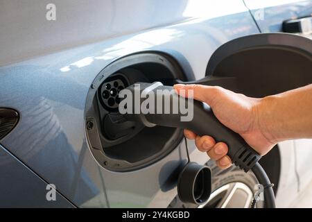 Ein Mann, der sein Elektroauto auflädt. Nahaufnahme seiner Hand, die den elektrischen Steckverbinder in das Fahrzeug einstecken soll. Stockfoto