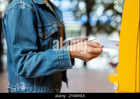 Eine Nahaufnahme einer Frau in einer Jeansjacke, die ihre Debitkarte in einen Geldautomaten einsteckt, um Geld abzuheben. Geldautomat, Mitarbeiter und Finanzdienstleister Stockfoto