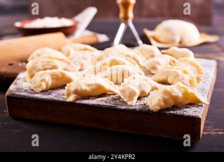 Rohe Vareniks mit Kartoffelfüllung auf einem Holzbrett auf dunklem Hintergrund. Das Konzept ist traditionelle ukrainische Küche. Horizontale Ausrichtung. Top-Film Stockfoto