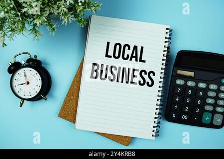 Lokaler Business-Text auf Papierkarte mit Taschenrechner und Wecker auf blauem Hintergrund geschrieben Stockfoto