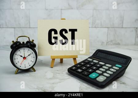 GST, Waren- und Dienstleistungssteuertext auf Papierkarte mit Taschenrechner und Wecker auf Marmorhintergrund geschrieben Stockfoto