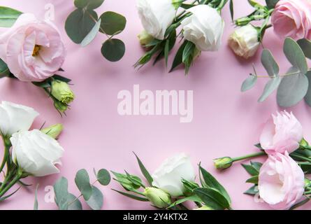 Frische pastellfarbene Rosen in Rosa- und Weißtönen sind elegant mit grünen Eukalyptusblättern auf einem weichen rosa Hintergrund angeordnet, perfekt für Dekorationen oder Stockfoto