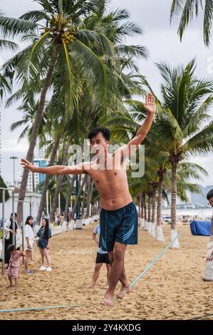 Ein asiatischer akrobat läuft an einem gestreckten Seil am Strand entlang, um Slackline zu trainieren. Nha Trang, Vietnam - 25. Juli 2024 Stockfoto