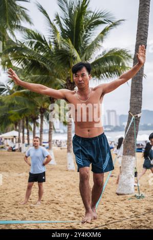 Ein asiatischer akrobat läuft an einem gestreckten Seil am Strand entlang, um Slackline zu trainieren. Nha Trang, Vietnam - 25. Juli 2024 Stockfoto